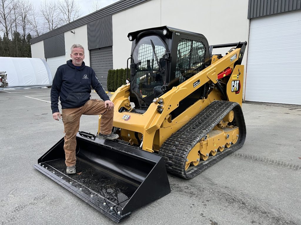 Bjorn Grimsmo, owner and founder of VIP Excavating, standing with a CAT 299D3 compact track loader at the VIP Excavating yard in the Fraser Valley